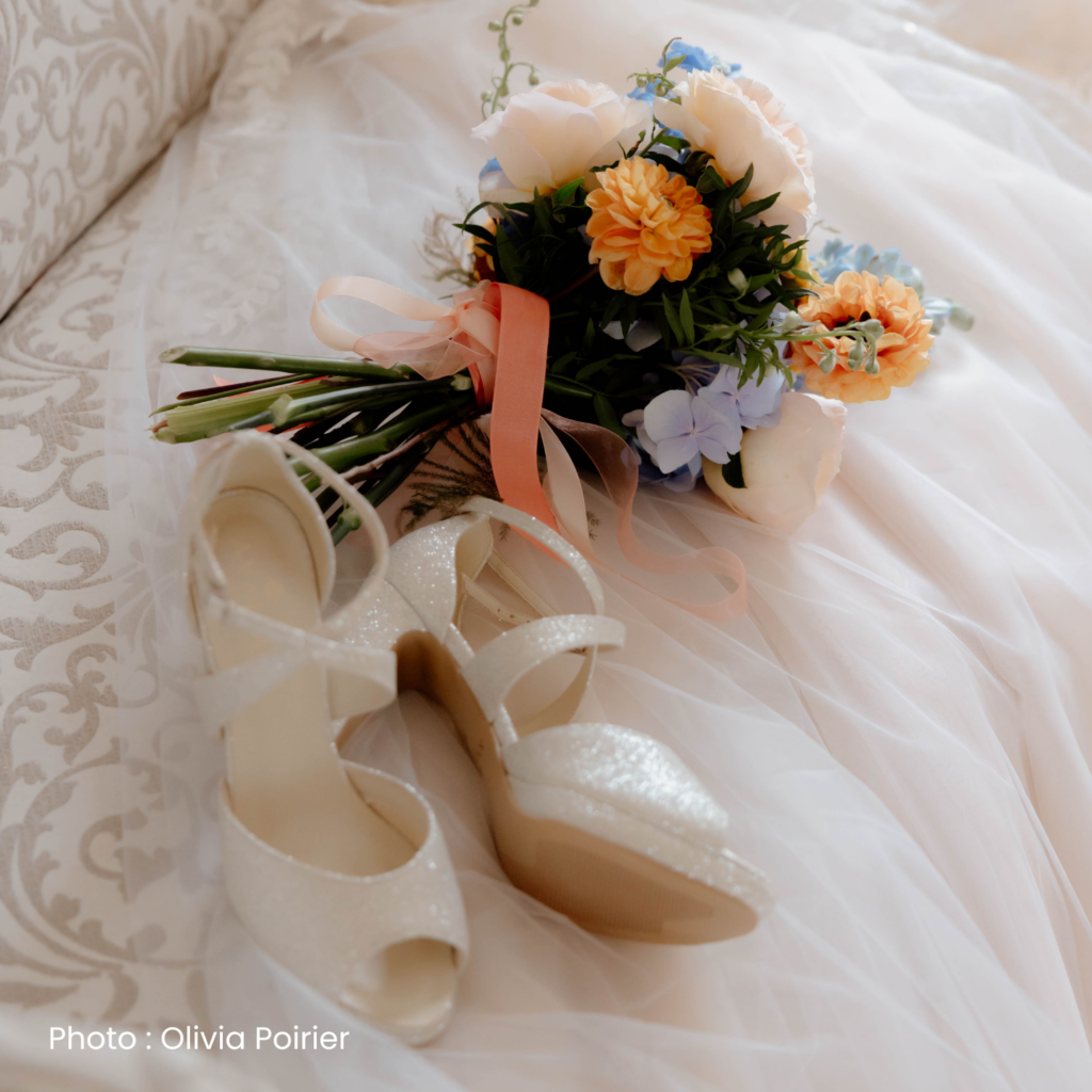 Chaussures de mariée pailletées et bouquet de fleurs oranges et bleues posés sur la robe, préparatifs de mariage en Mayenne